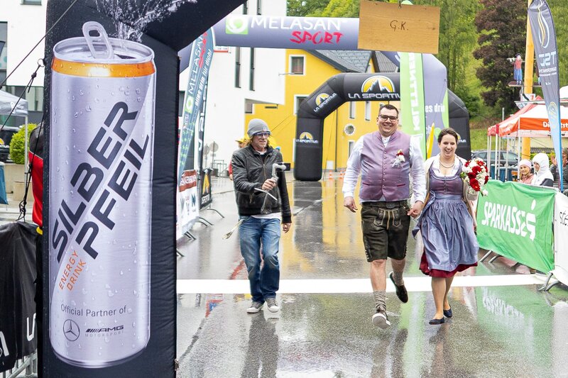Ein Paar in Tracht läuft Hand in Hand durch den Zielbogen