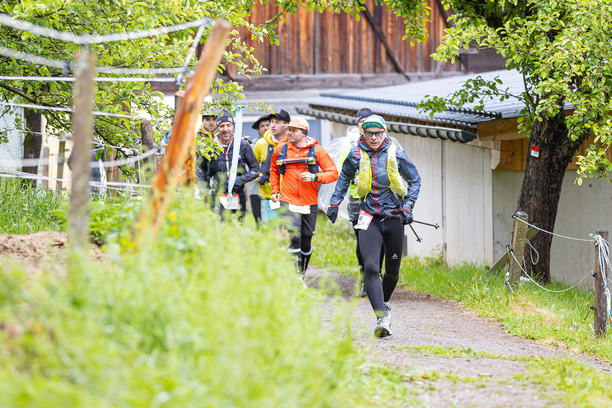 Trailläufer unterwegs auf einem schmalen Weg zwischen Obstbäumen und Bauernhof
