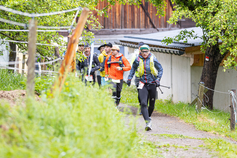 Trailläufer unterwegs auf einem schmalen Weg zwischen Obstbäumen und Bauernhof